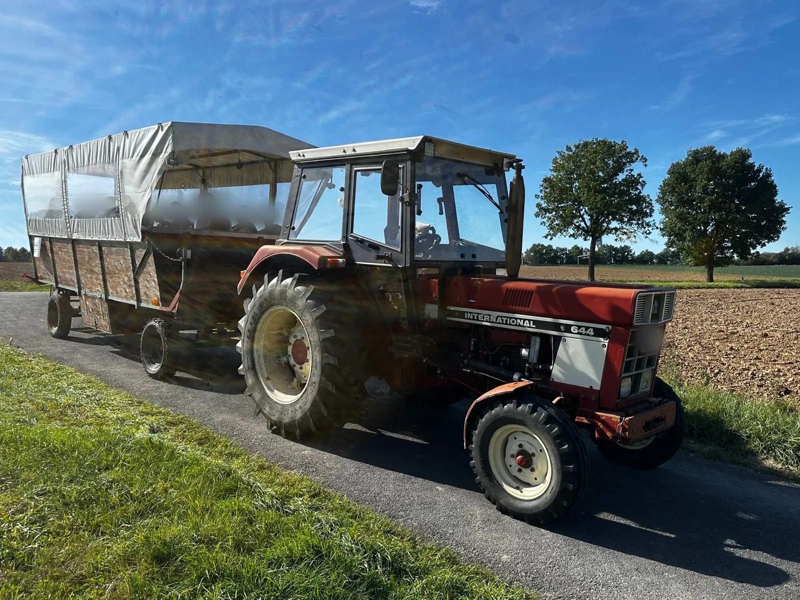 Der Traktor zieht den besetzten Planwagen über einen Feldweg zwischen Wiese und Acker